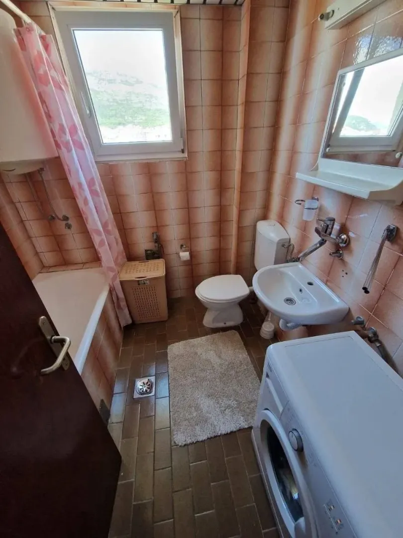 Small bathroom with a bathtub, sink, and washing machine tiled with ceramic tiles.