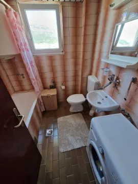 Small bathroom with a bathtub, sink, and washing machine tiled with ceramic tiles. - image 5