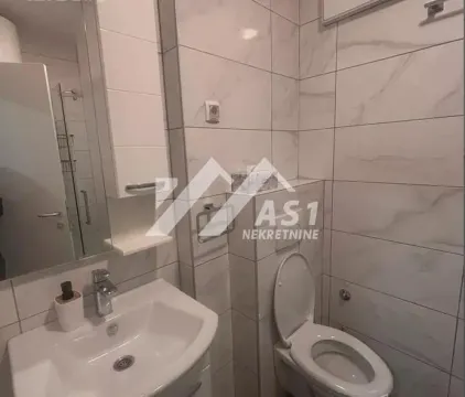 Manje kupatilo obloženo svetlim pločicama sa umivaonikom i toaletnom šoljom. - image 7