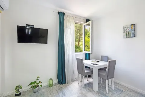 Living room with a dining table, wall-mounted TV, and a window overlooking greenery. - image 2