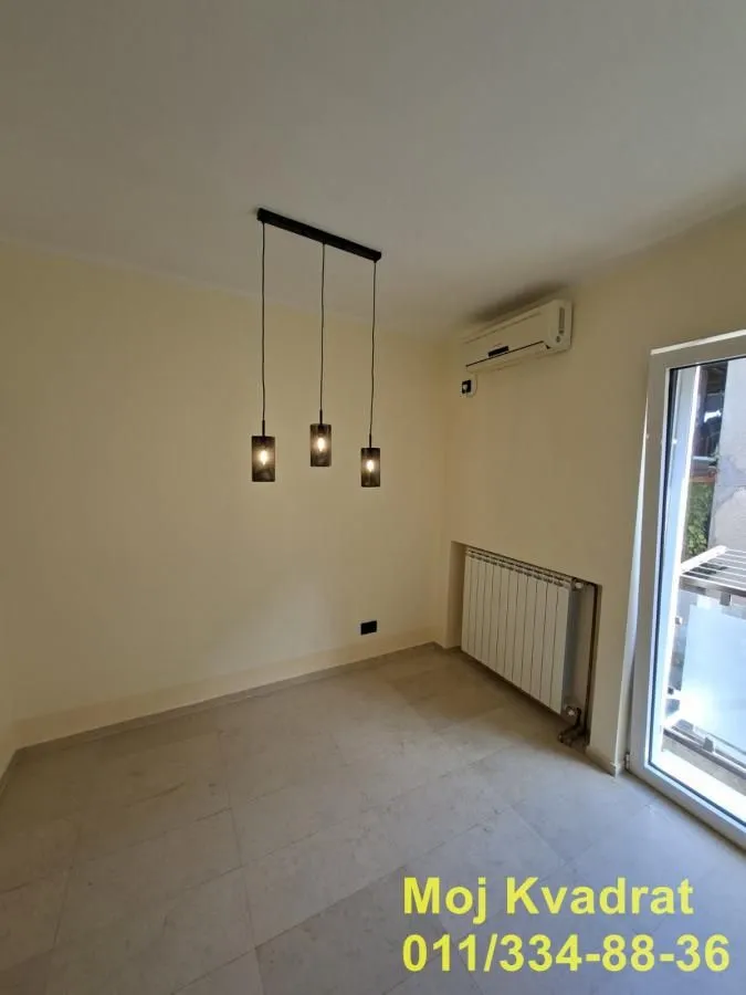 Prazna soba sa klima uređajem, radijatorom i modernim lusterom.
