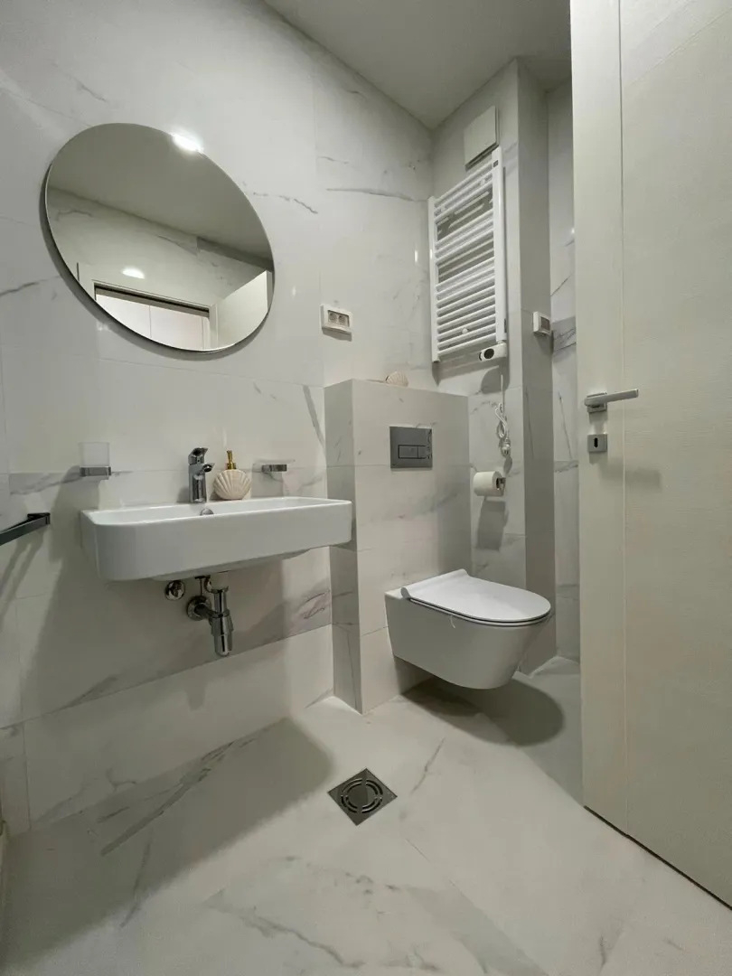 Moderna i svijetla kupatila sa umivaonikom, WC šoljom i okruglim ogledalom.