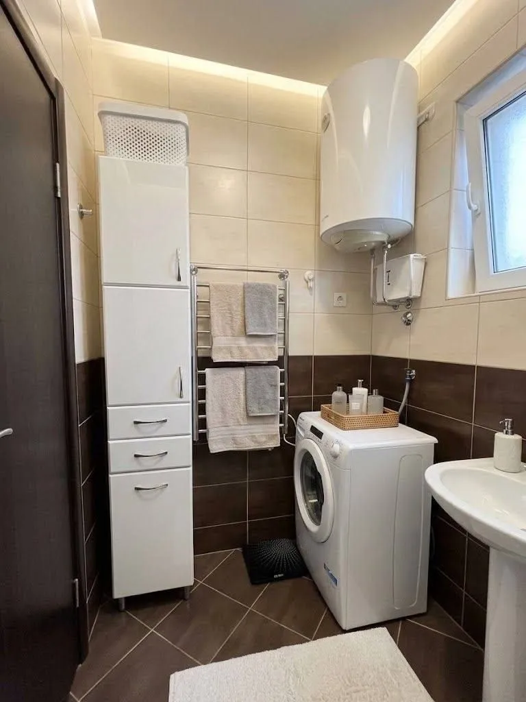 Pregledno kupatilo sa bijelim elementima, veš mašinom i bojlerom.