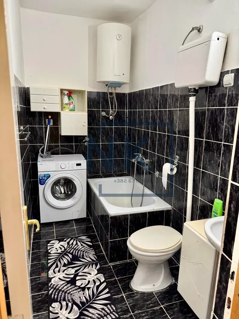 Small bathroom with black tiles, bathtub, washing machine, and water heater.