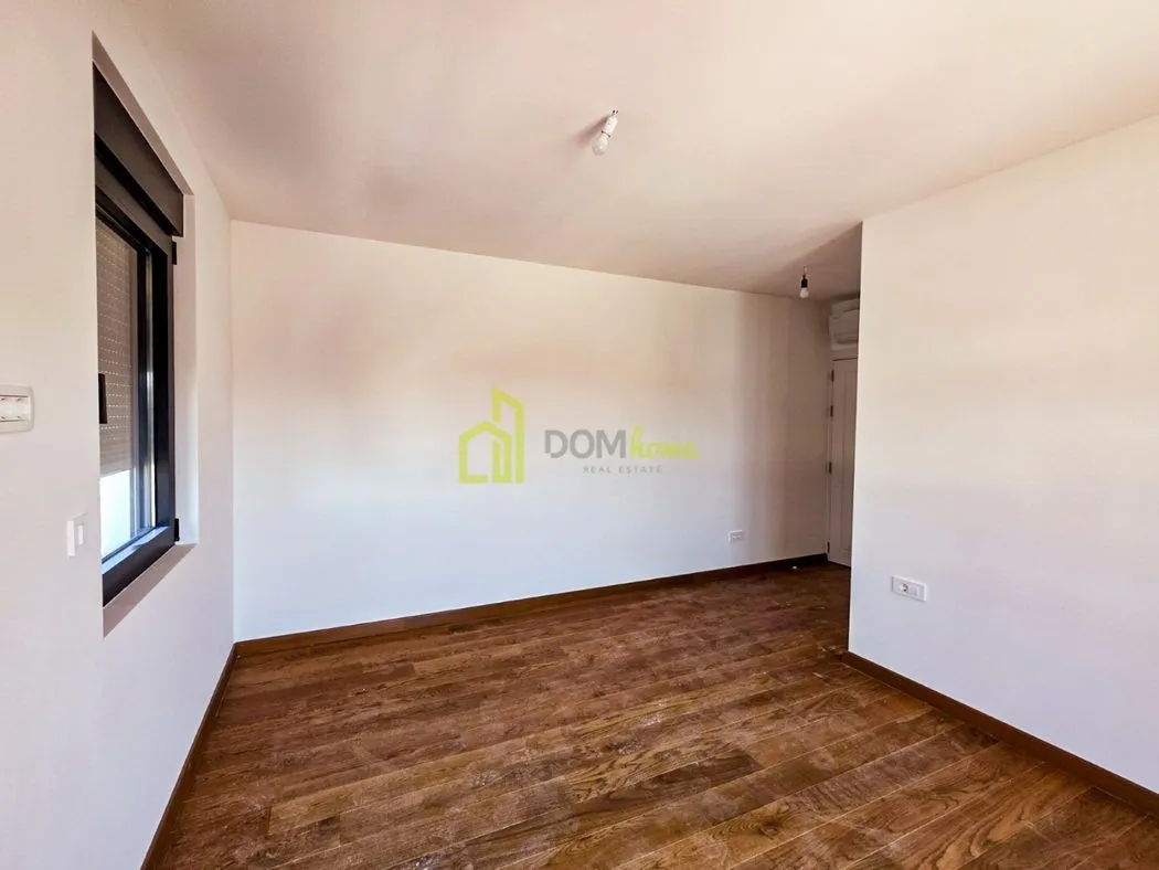 Empty room with white walls, wooden flooring, and a window with roller blinds.
