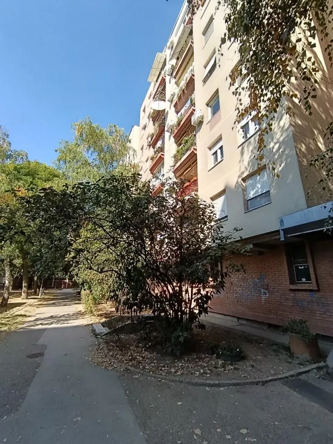 Pogled na spoljašnjost zgrade sa zelenilom i stazom ispred ulaza.