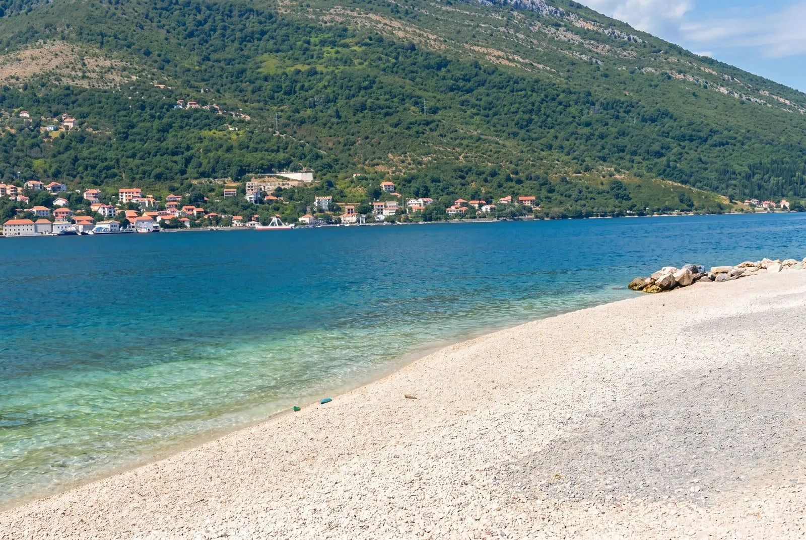Pogled sa šljunkovite plaže na more i planine.