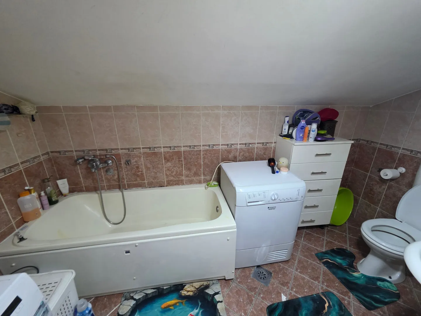 Manje kupatilo sa kadom, veš mašinom, komodom i toaletom.