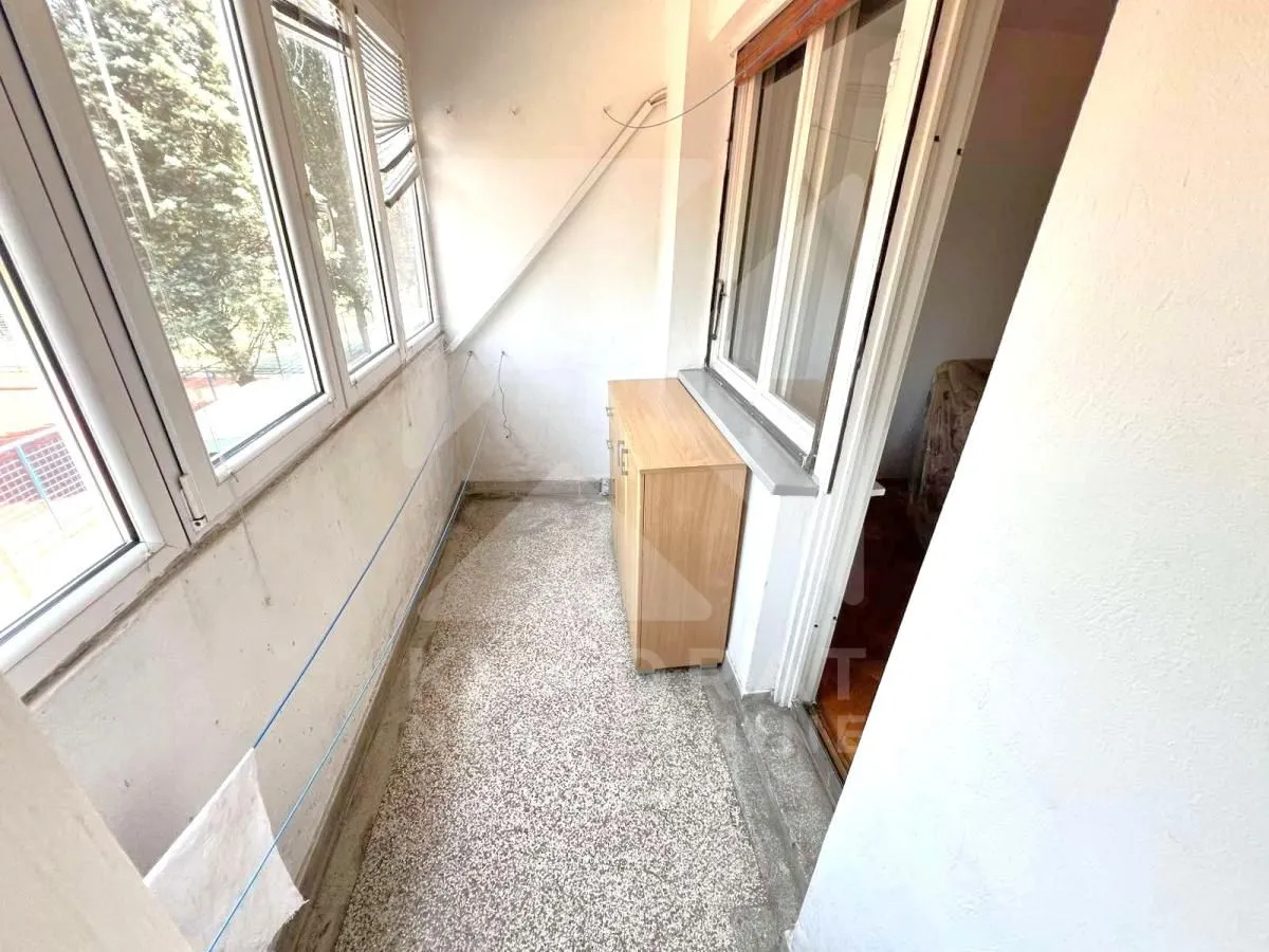 Zastakljeni balkon sa velikim prozorima i drvenom komodom.