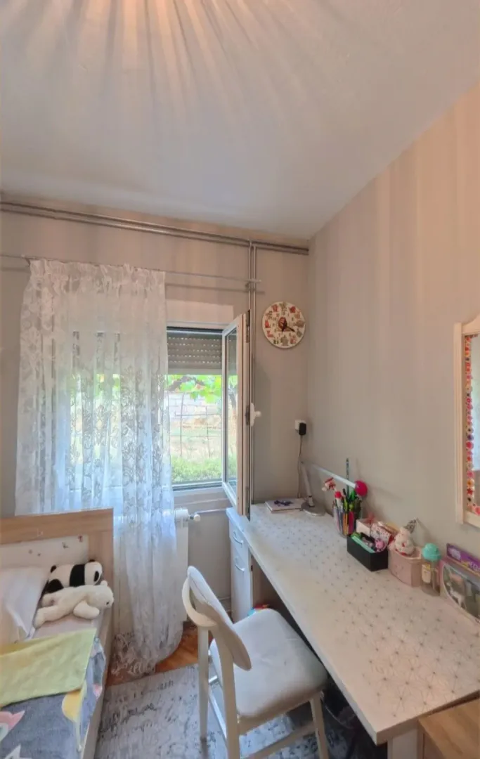 Dječja soba sa krevetom, radnim stolom i prozorom koji gleda na dvorište.