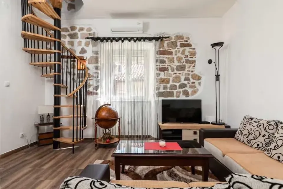 Living room with a sofa set, spiral staircase, and an exposed stone wall feature.