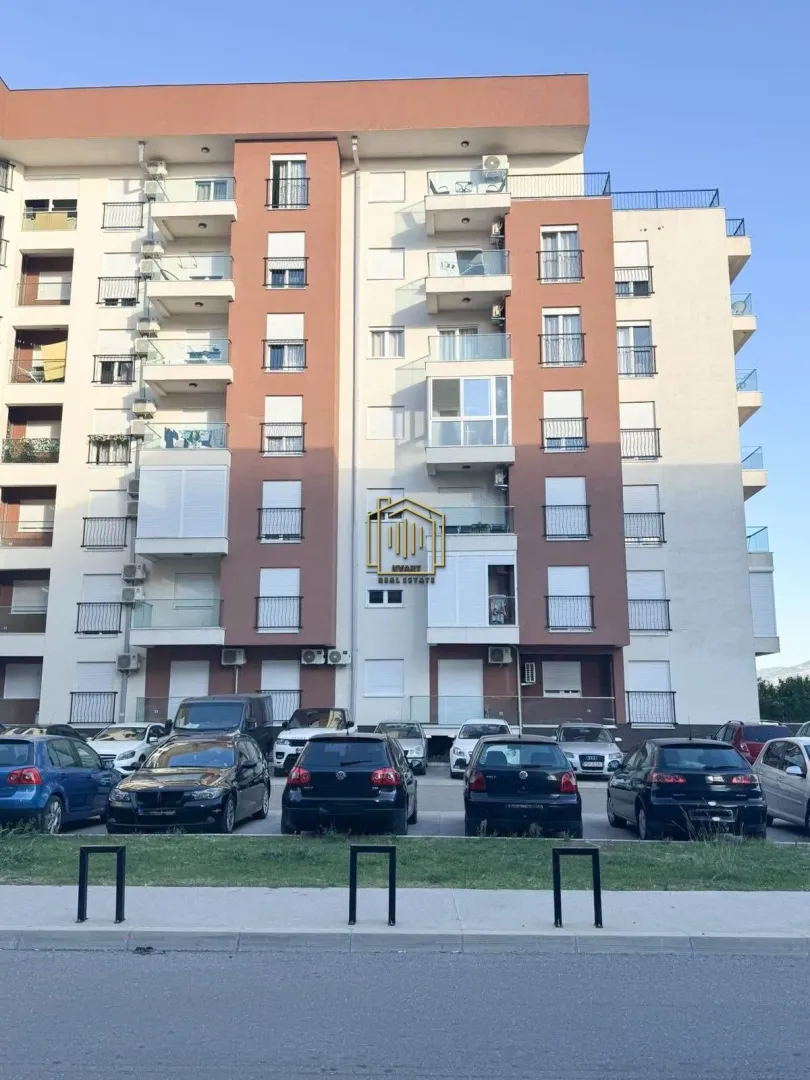 Pogled na fasadu stambene zgrade sa parkingom u prvom planu.
