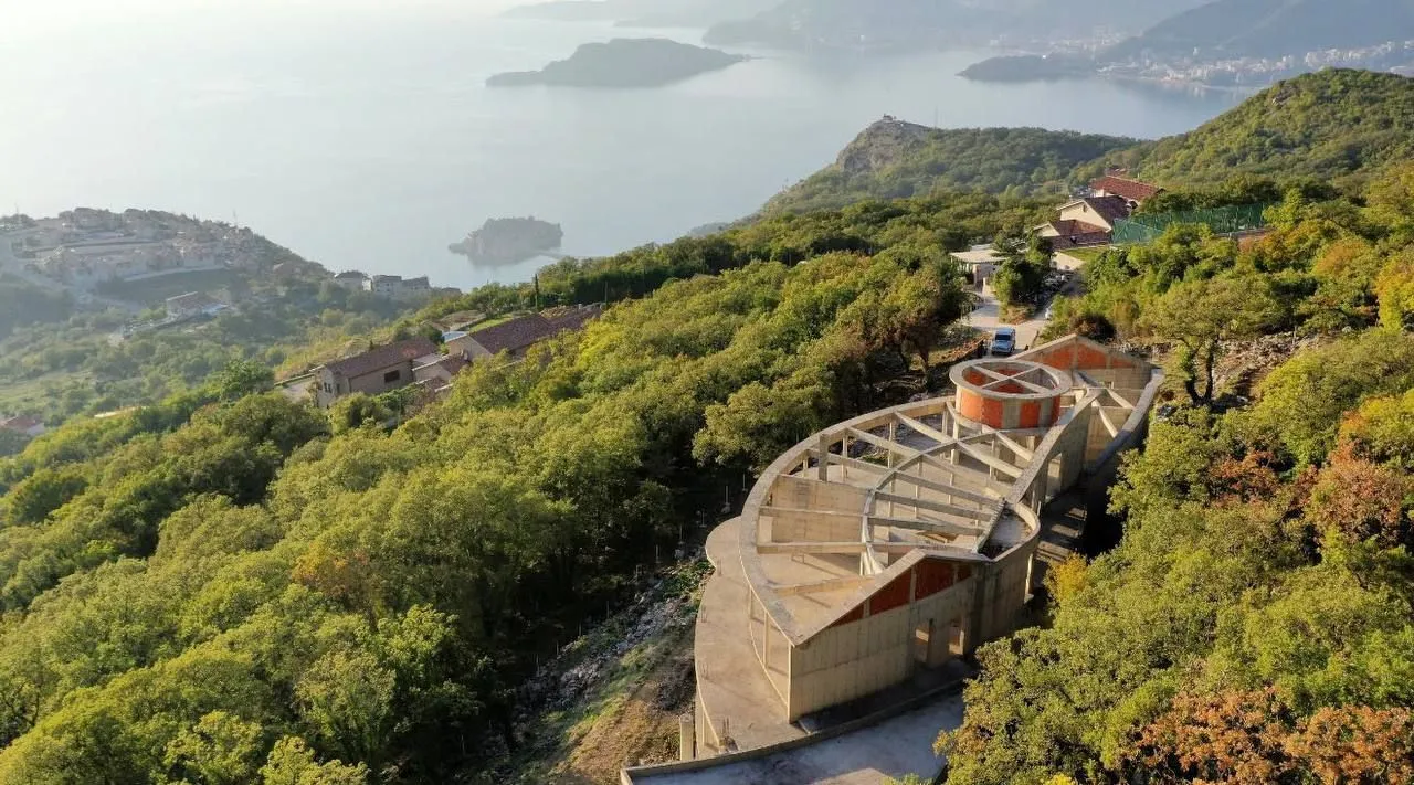 Pogled iz vazduha na objekat u izgradnji okružen zelenilom sa pogledom na more.