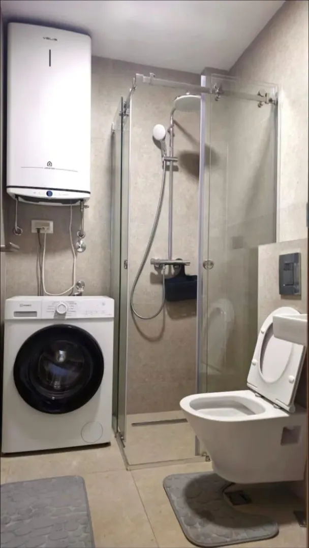 Modernly equipped bathroom with a shower cabin, toilet, washing machine, and water heater.