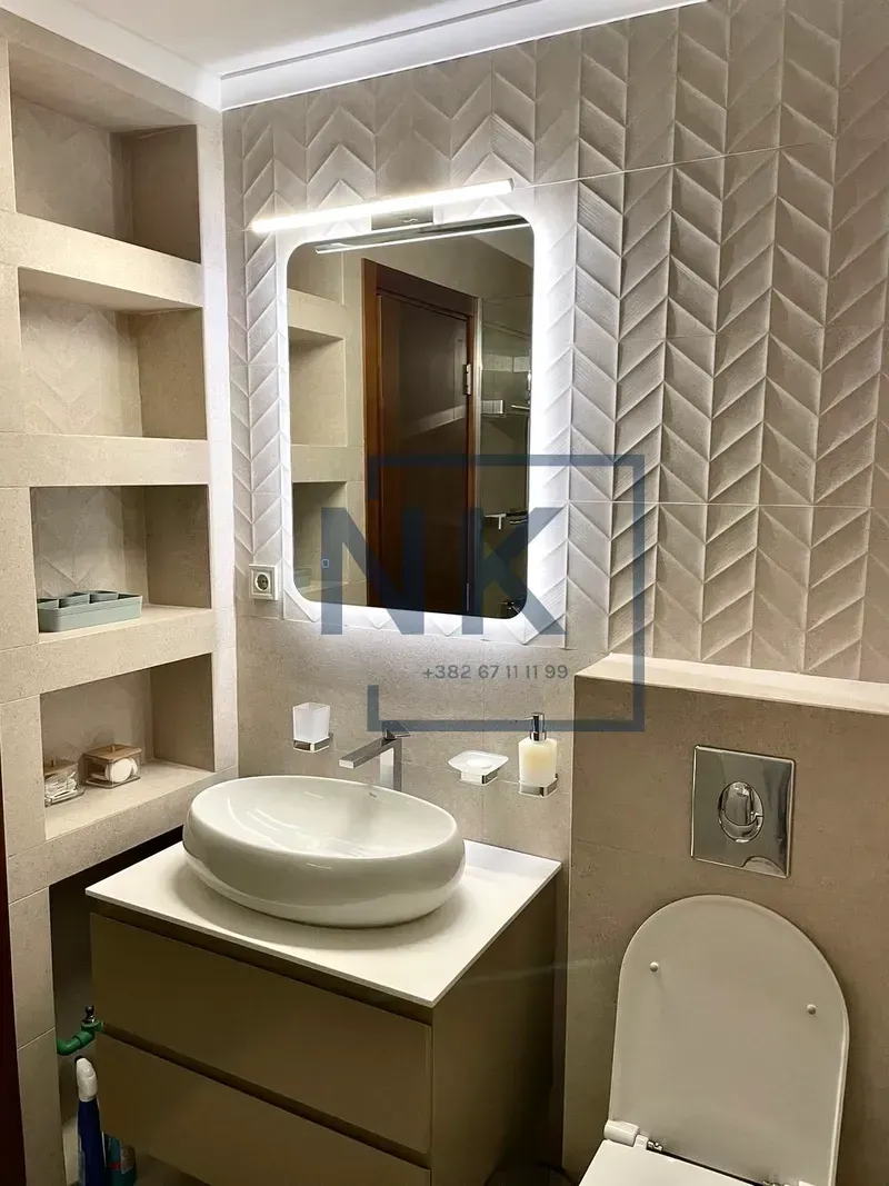 Modern bathroom with a washbasin, illuminated mirror, and built-in shelves.