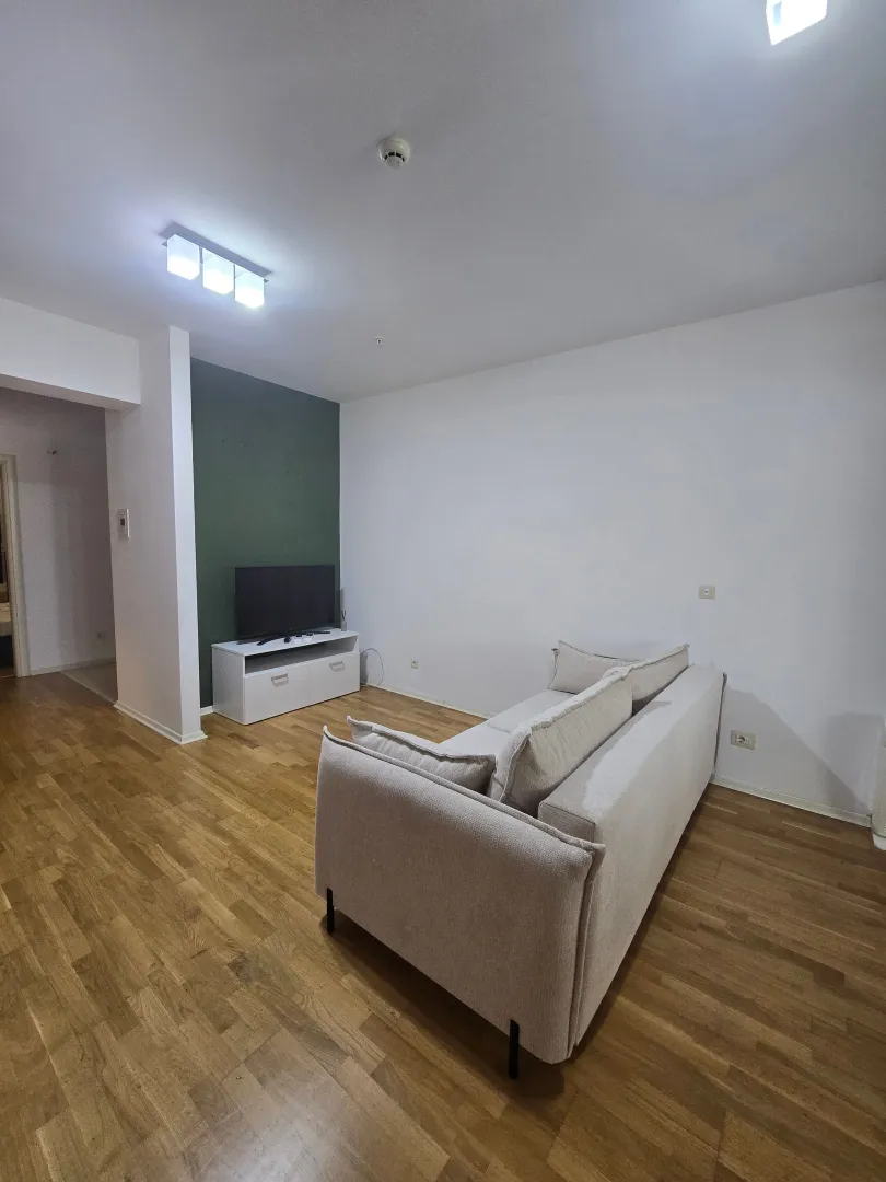 Dnevna soba sa svijetlom garniturom, TV komodom i drvenim podom.