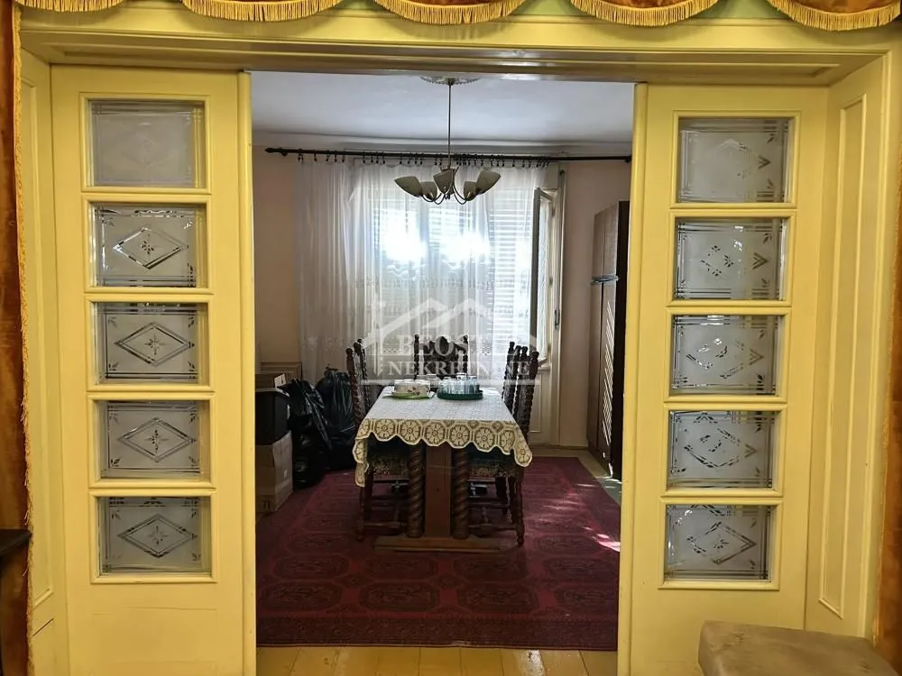 Pogled kroz dvokrilna vrata na trpezariju sa stolom i crvenim tepihom.