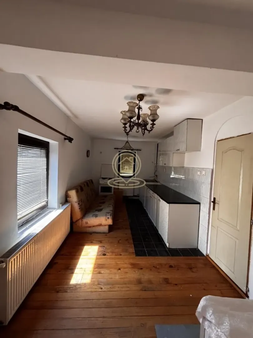 Long kitchen with wooden floor, sofa and white cabinets.