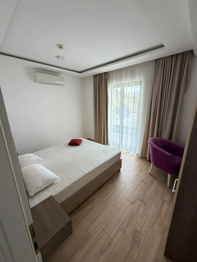 Svjetla spavaća soba sa bračnim krevetom i ljubičastom foteljom.