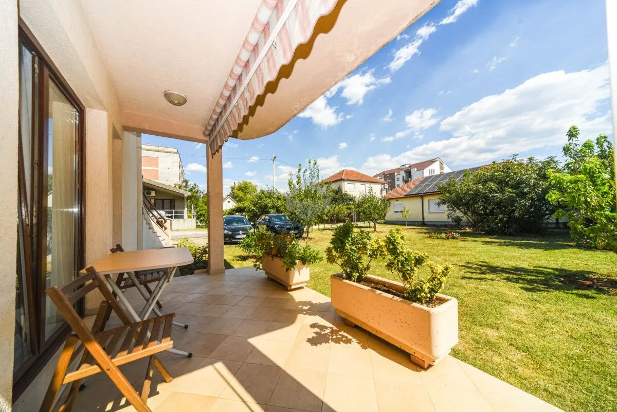 Covered terrace with a table and chairs and a view of the grassy yard.