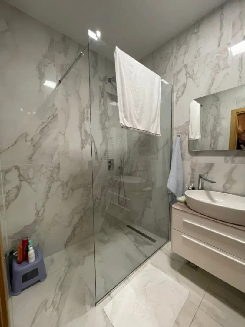 Bright bathroom with a glass shower cabin and marble-patterned tiles.