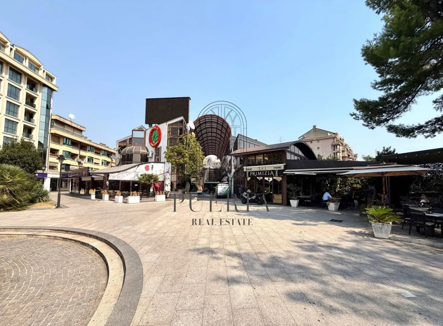 View of a paved square with commercial buildings and cafes.