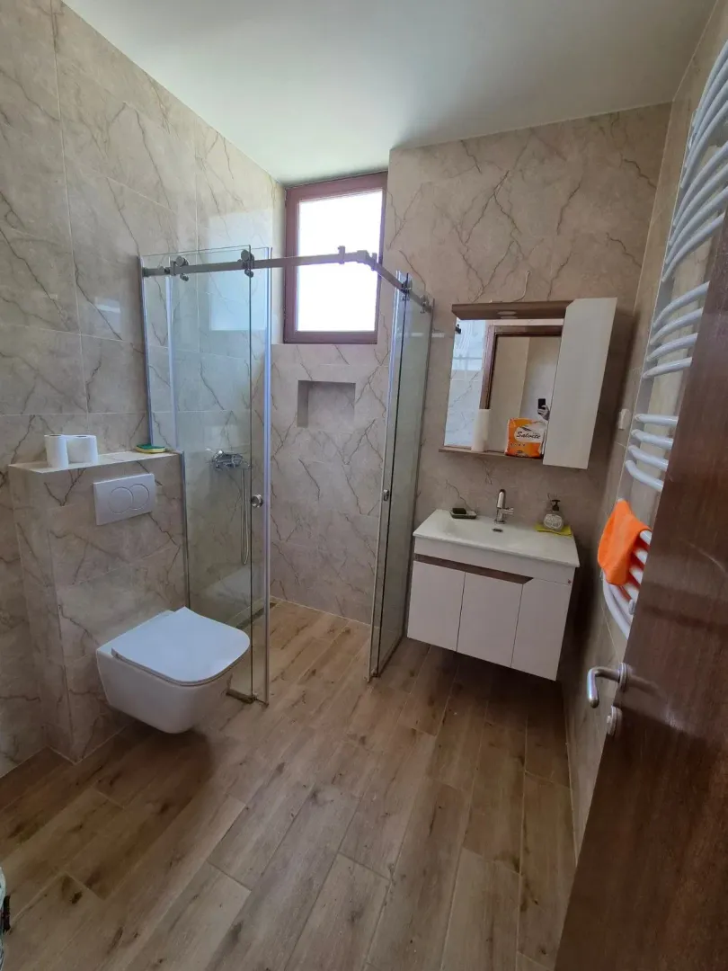 Moderno kupatilo sa tuš kabinom, umivaonikom i ugrađenom wc šoljom.