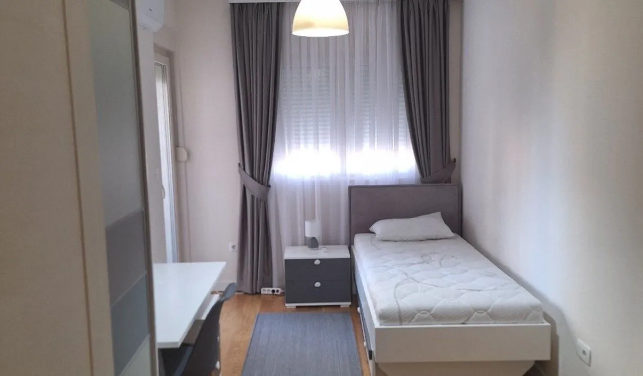 Manja spavaća soba sa krevetom za jednu osobu, noćnim stočićem i radnim stolom.