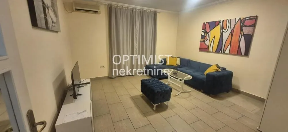 Dnevna soba sa garniturom, televizorom i umetničkom slikom na zidu.
