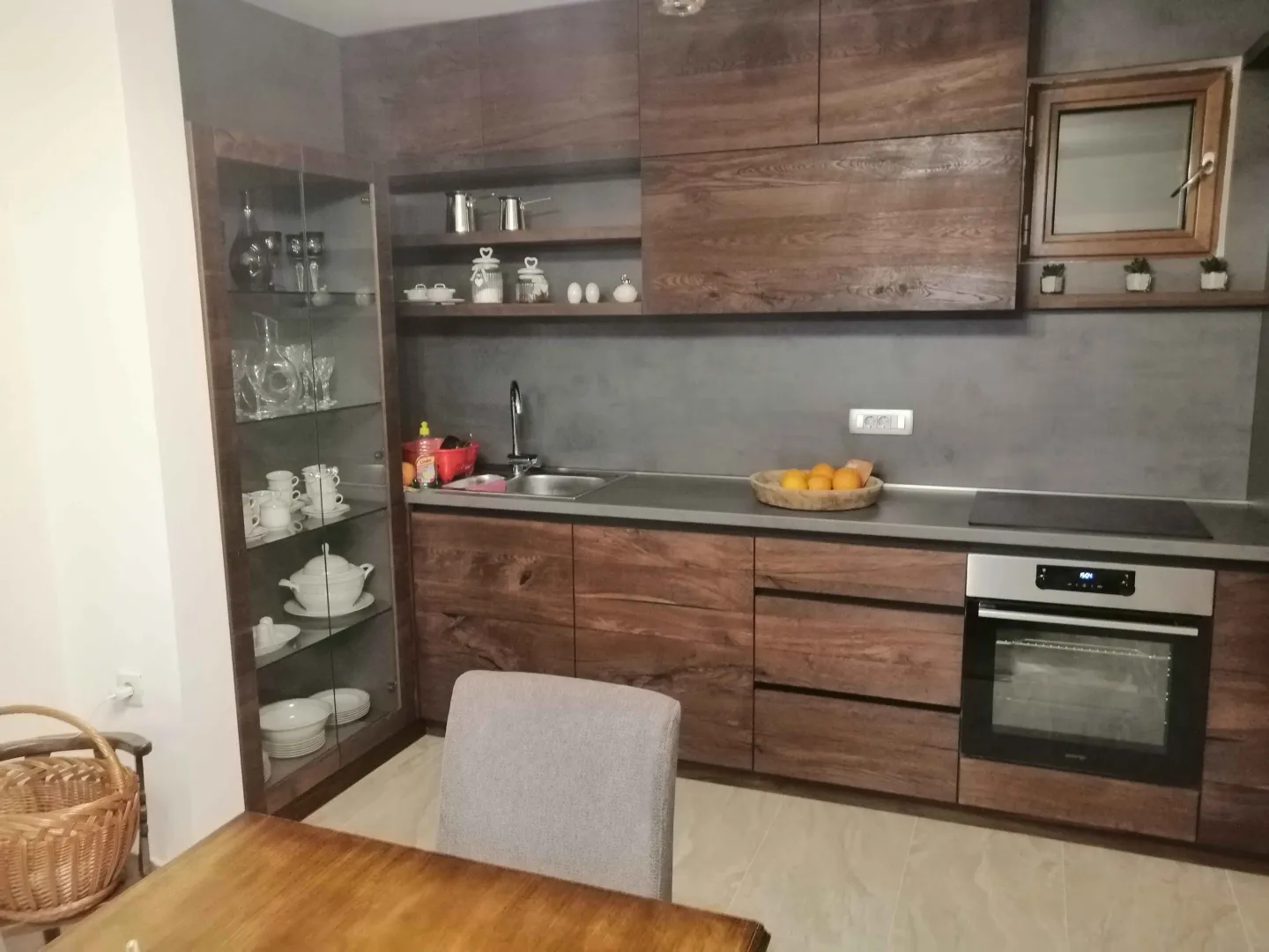 Kuhinja opremljena tamnim drvenim elementima i ugrađenom rernom.
