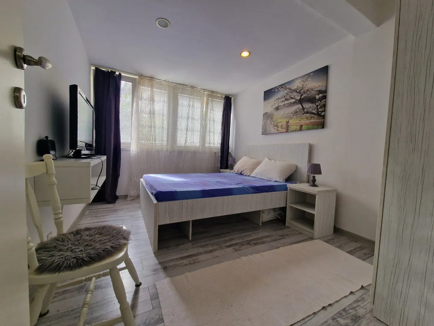 Furnished bedroom with a double bed, television, and window.