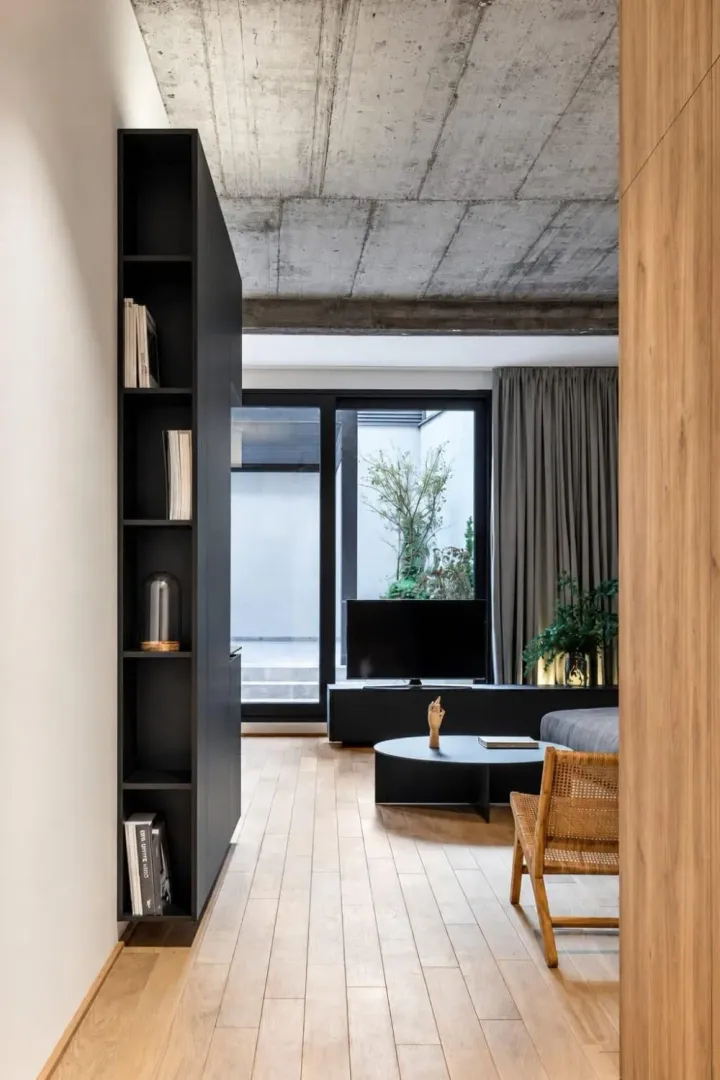 View from the hallway into a modern living room with a concrete ceiling and black elements.