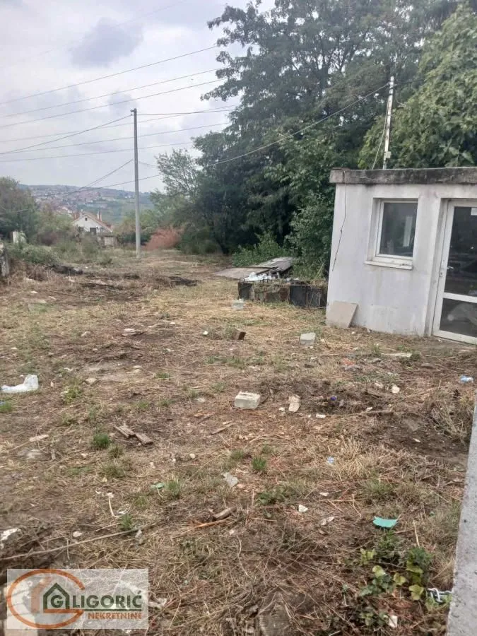 Pogled na plac sa manjim pomoćnim objektom i rastinjem.