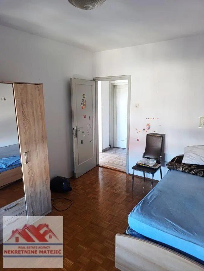 Furnished bedroom with a bed, wooden wardrobe, and parquet flooring.