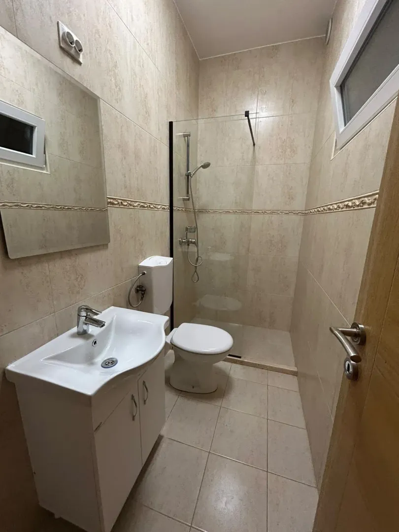 Small bathroom with a walk-in shower, washbasin, and toilet, tiled with ceramic tiles.