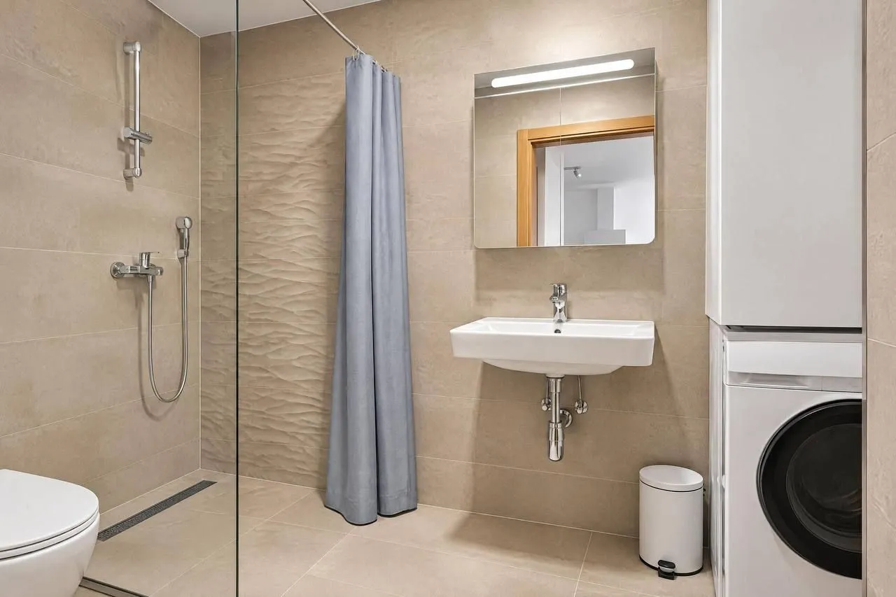 Modern bathroom with a walk-in shower, washbasin, mirror, and washing machine.