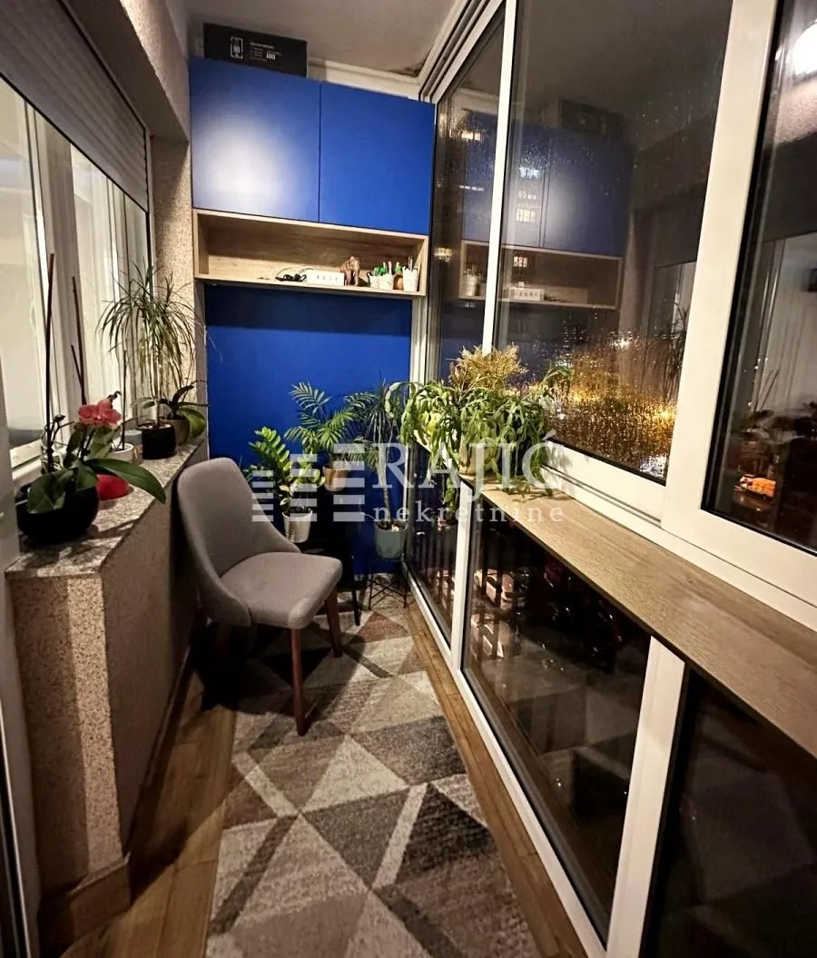 Enclosed balcony with a rug, chair, cabinetry, and potted plants.