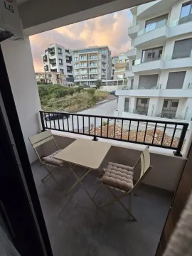 Small furnished balcony with a table and two chairs and a view of buildings. - image 14