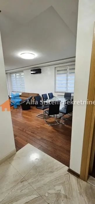 Pogled iz predsoblja na prostrani dnevni boravak sa trpezarijom i garniturom za sedenje.