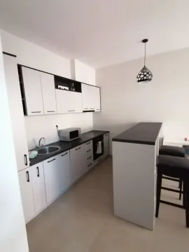 Moderna kuhinja sa bijelim elementima, šankom i crnim barskim stolicama. - image 4