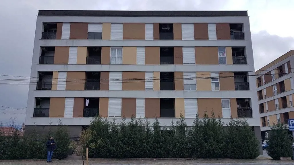View of the front facade of a multi-story residential building with terraces and roller shutters.