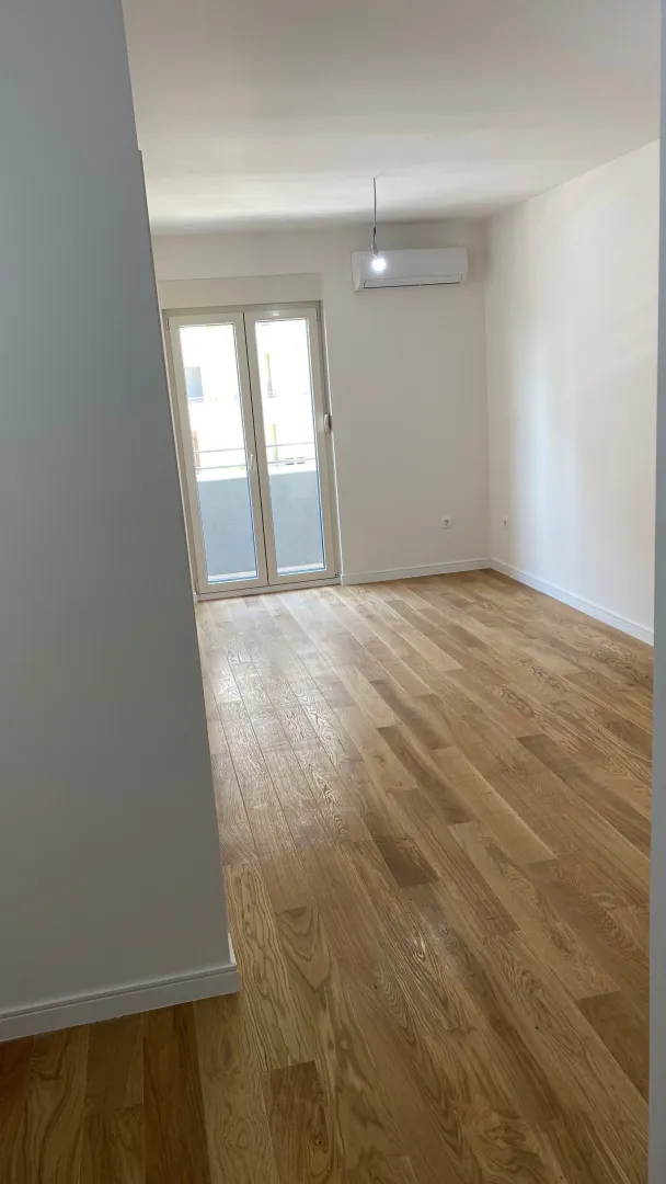 An empty room with light wood parquet, air conditioning, and access to a balcony.