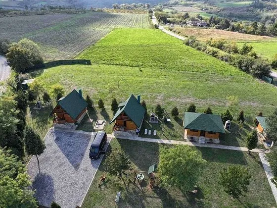 Pogled iz vazduha na drvene kućice u prirodi sa velikim dvorištem i zelenilom.