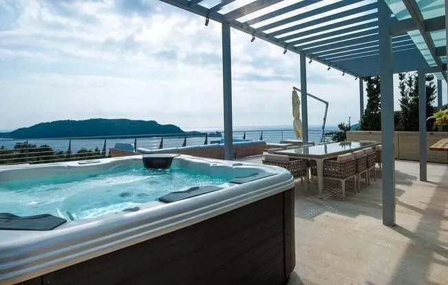 Spacious covered terrace with a jacuzzi, dining table, and sea view.