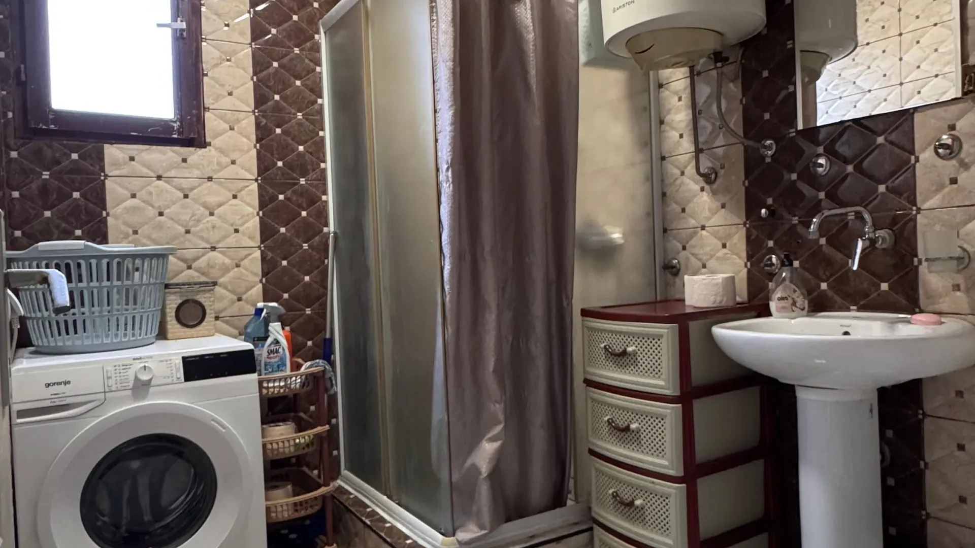 Compact bathroom with a shower cabin, sink, washing machine, and water heater.