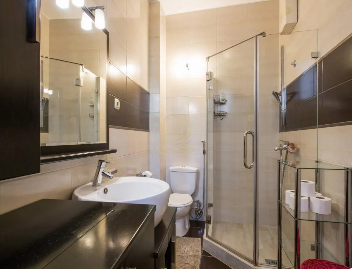 Kupatilo opremljeno umivaonikom, WC šoljom i tuš kabinom sa staklenim paravanom.