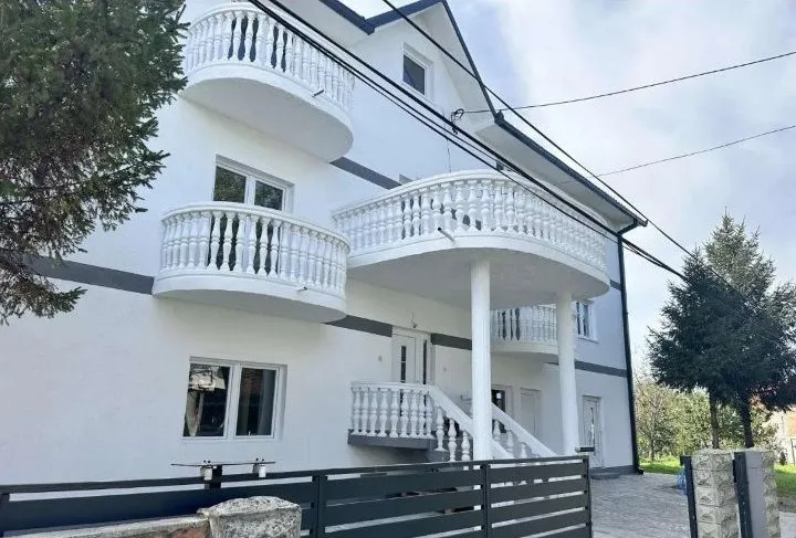 Eksterijer bele kuće sa više balkona i ogradom.