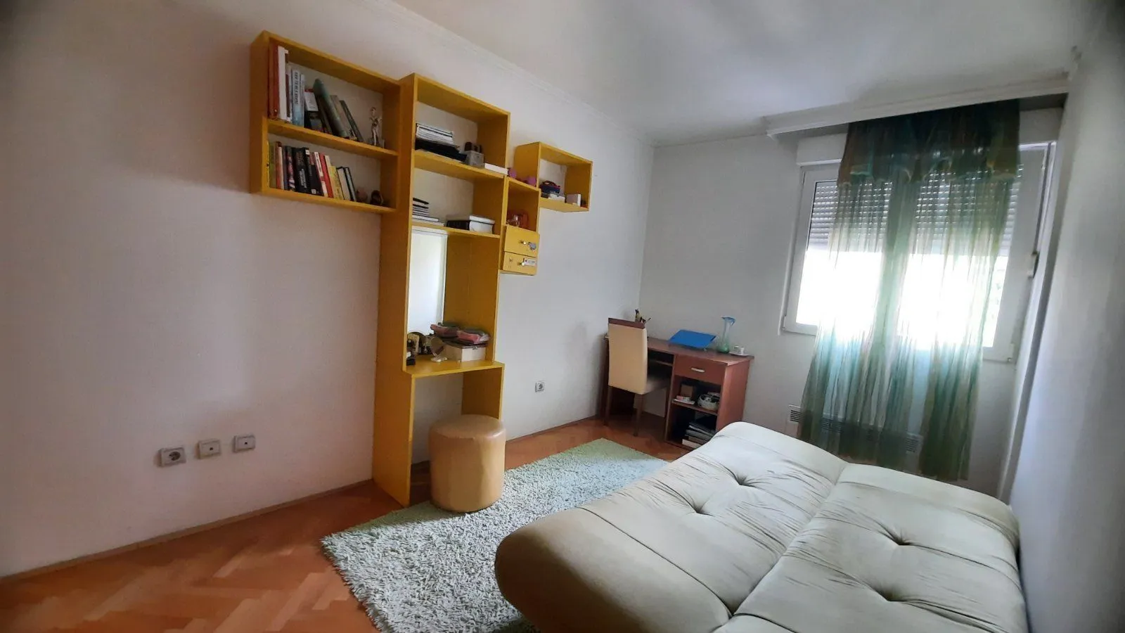 A bright room with yellow shelving, a desk, and a bed.