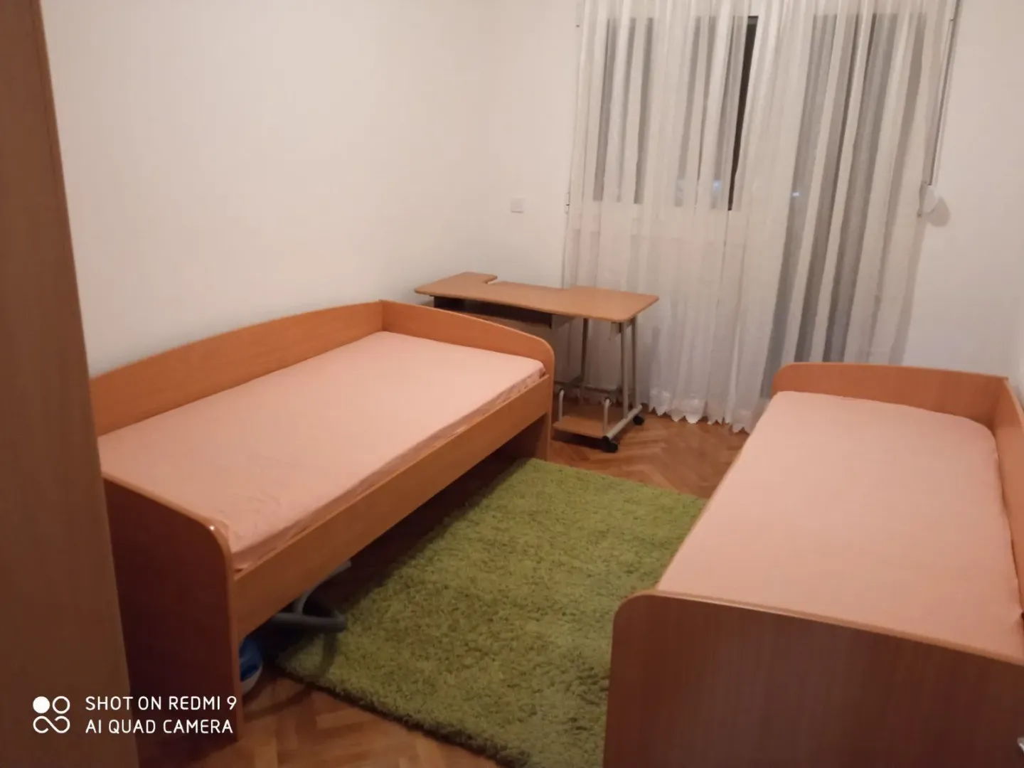 A bedroom with twin beds, a desk, and a green rug.
