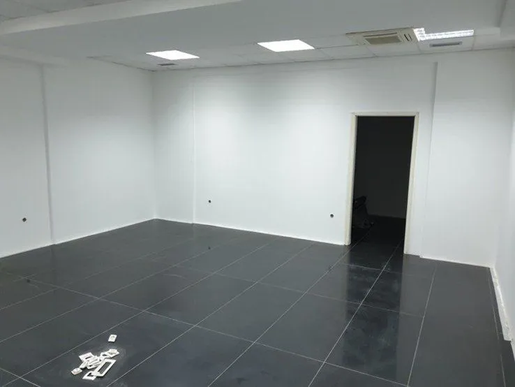 Empty office space with white walls and dark floor tiles.